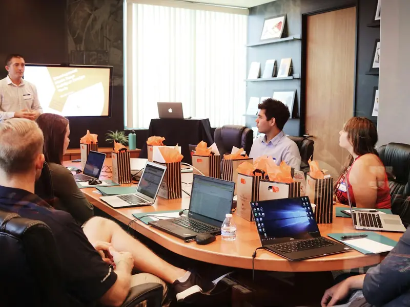 A project team meeting around a table with laptops and a presentation screen