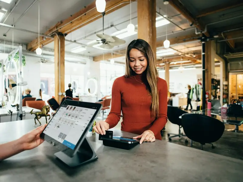 A cashier serving a customer at a store counter with a tablet till