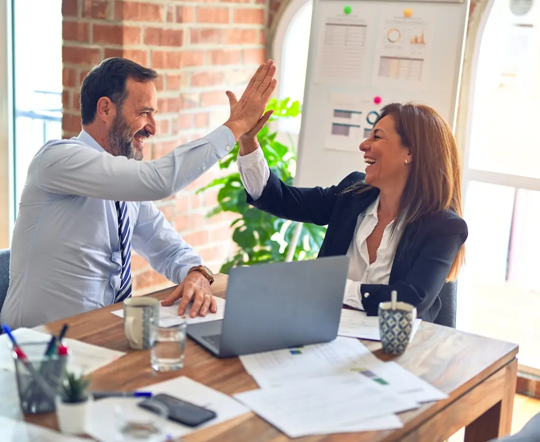 Two colleagues high-fiving across a desk in a bright office
